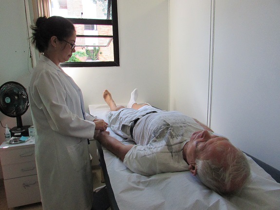 Acupunturista massageia mão esquerda de paciente deitado em maca.