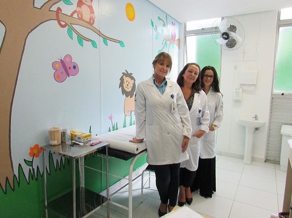 Profissionais na sala de pediatria.À esquerda, uma parede pintada com desenhos para crianças