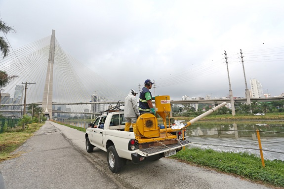 Agentes de saúde, a bordo de uma caminhonete, aplicam inseticida à margem do Rio Pinheiros 