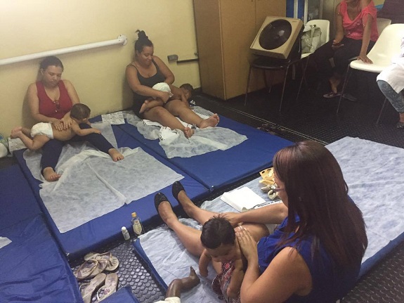 Mães sentadas em colchões azuis fazem massagem em bebês 