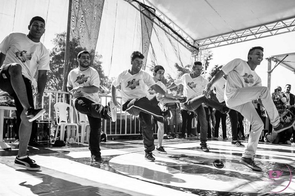 Foto em preto e branco. Grupo de jovens dança no palco improvisado.
