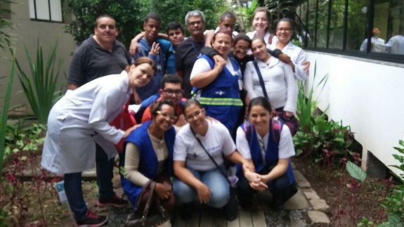 No jardim com árvores e mudas, agentes de saúde, pacientes e enfermeiras posam para a foto. 