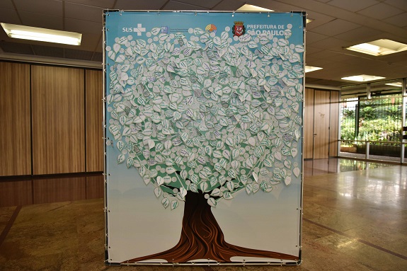 No saguão do evento, a Árvore dos Desejos com pétalas de papel brancas e palavras escritas em verdeexibe sugestões e expectativas dos participantes em relação à saúde na cidade de São Paulo