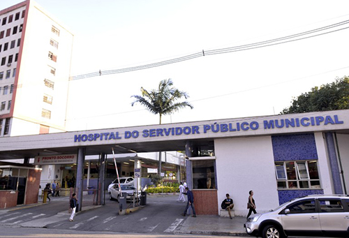 Fotomostra entrada do HSPM com suas duas guaritas e o letreiro com o nome do hospital em letras azuis.