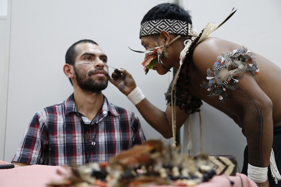 Índio pinta o rosto de um participante com traços pretos e delicados