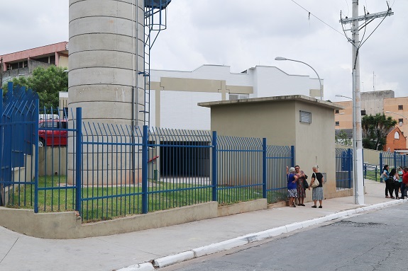 A foto traz a fachada da unidade Pro Morar nas cores branco, cinza e bege, com cercas de ferro em azul royal