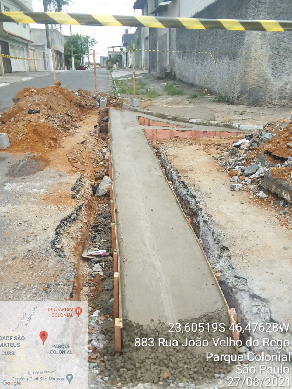 Metade do sarjetão de uma rua está com concreto novo, ainda com as escoras.  Ao lado, valetas  e ao fundo, um monte de terra e entulho. 