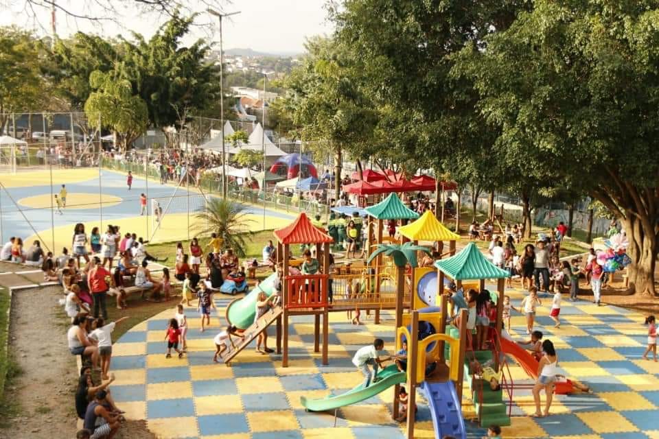 Foto da Praça do Samba, há um playground em formato de castelo aberto com escorregadores coloridos, há diversas crianças brincando, ao fundo pode se observar as tendas da feira de artesanato e a quadra de futebol.