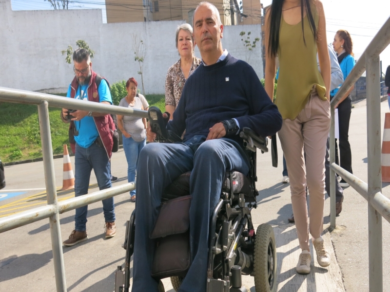 Secretario da pessoa com deficiência subindo com cadeira de rodas a rampa de entrada da subprefeitura Cidade Tiradentes e acompanhado por servidores da Prefeitura de Saõ Paulo