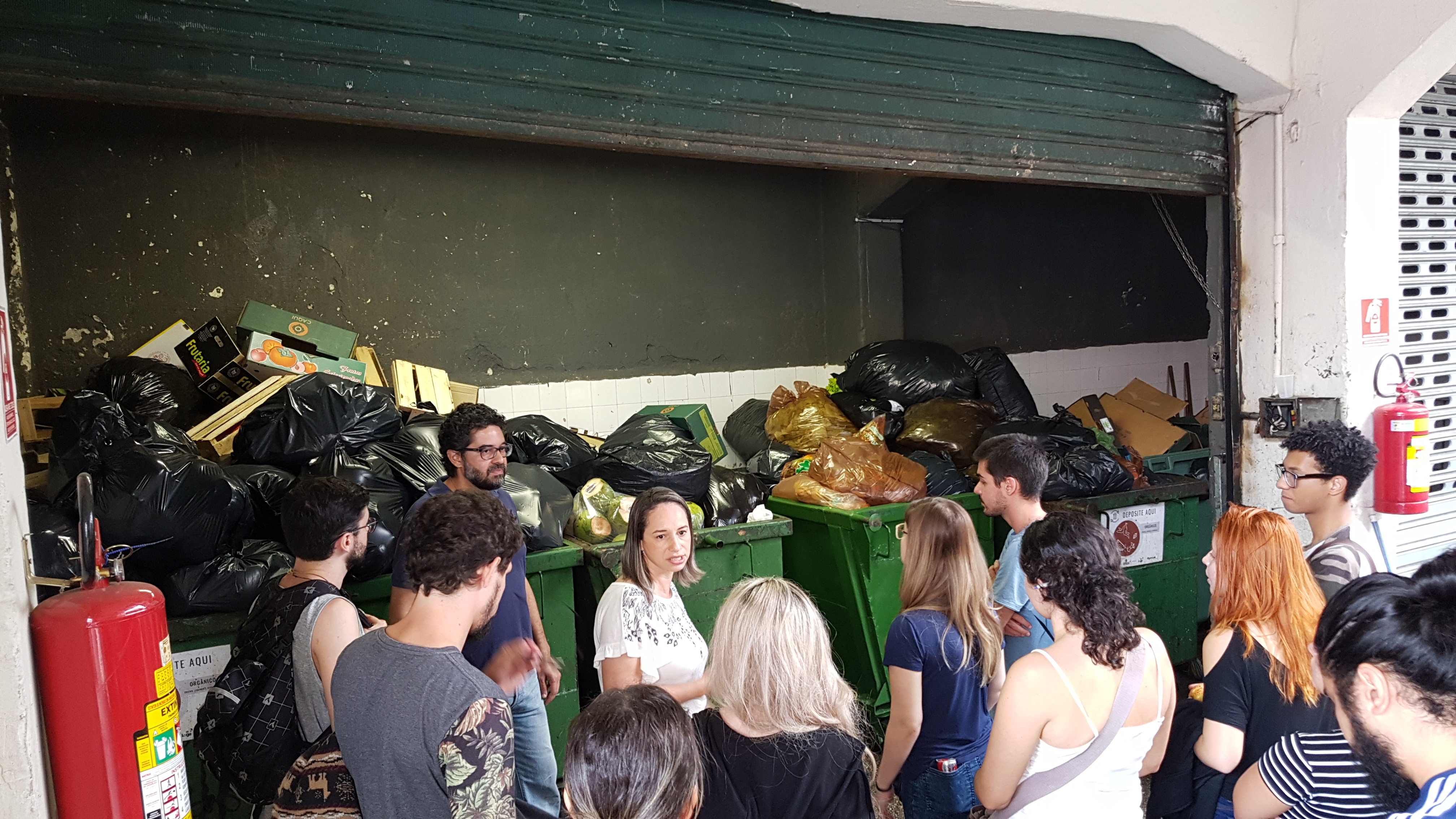 Maria Piedade conversa com os alunos. Todos estão em frente as lixeiras do Mercado Kinjo.