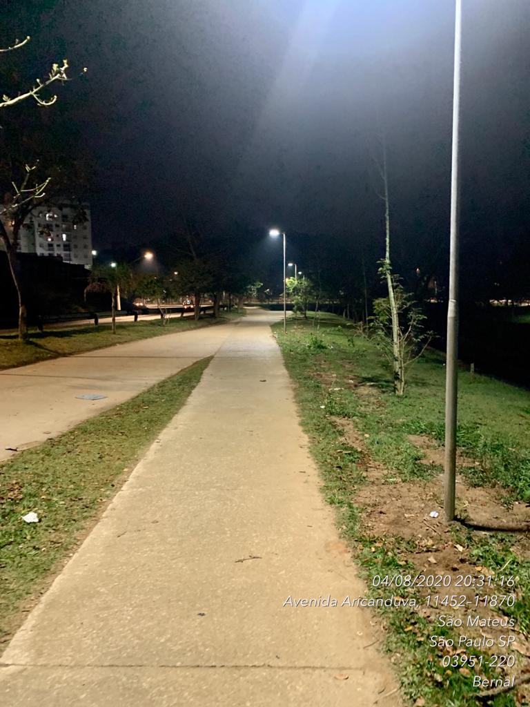 faixa de concreto de uma pista de caminhada está iluminada, com o gramado verde ao lado.