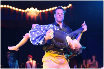Criança e pai no palco de um espetáculo, criança está erguida nos braços do adulto, ambos com vestimentas circenses 