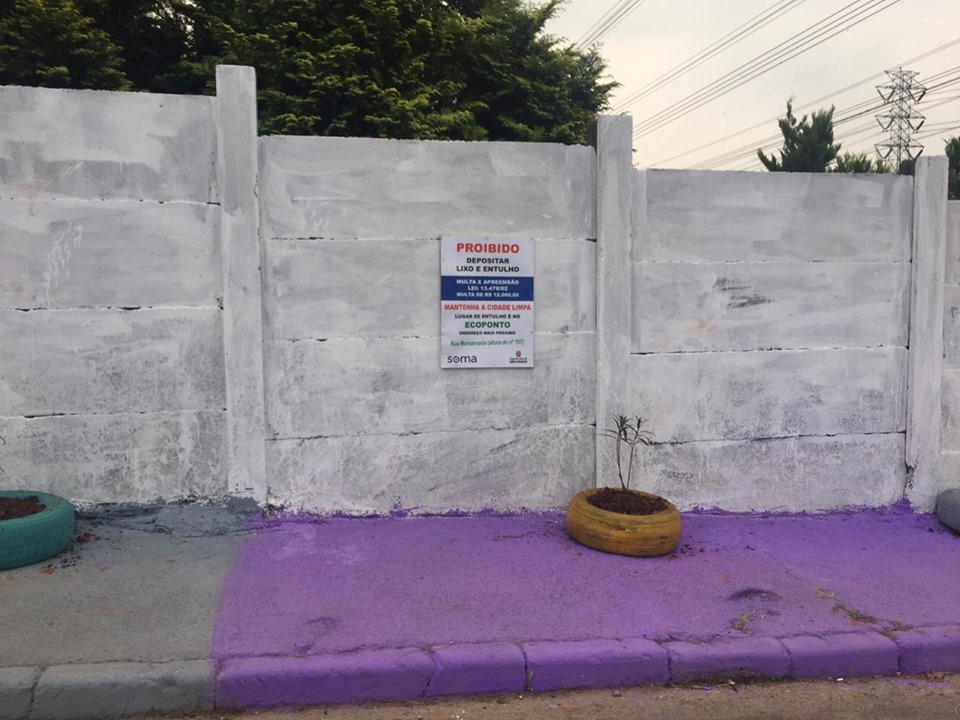 Calçada pintada de roxo e uma placa na parede com os dizeres: proibido depositar lixo.