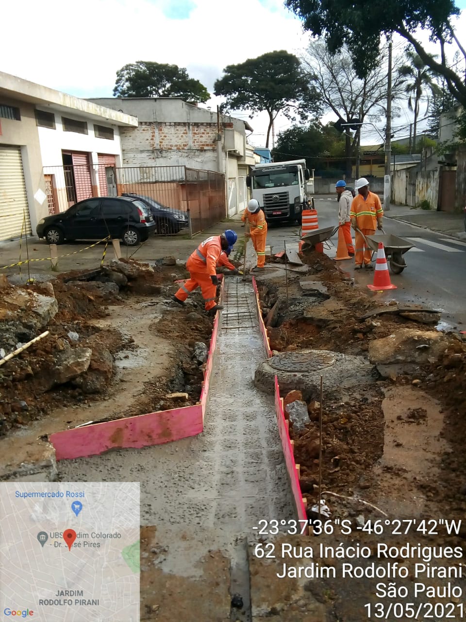 Quatro trabalhadores com macacão laranja concluem concretagem de um sarjetão, em foto identificada como rua Inácio Rodrigues, Jardim Rodolfo Pirani.