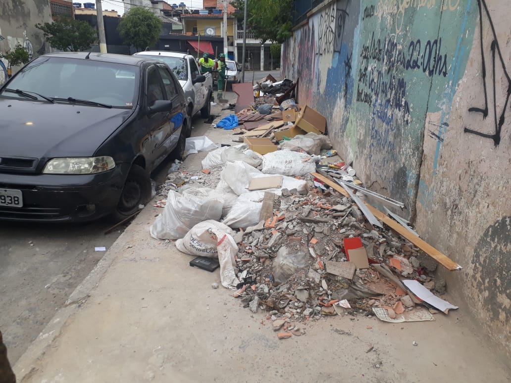 Imagem do antes da revitalização. O muro na lateral direita está todo pichado. No centro da imagem a calçada está cheia de entulho, de maneira que é impossível o tráfego de pessoas, ao lado há um carro preto estacionado.