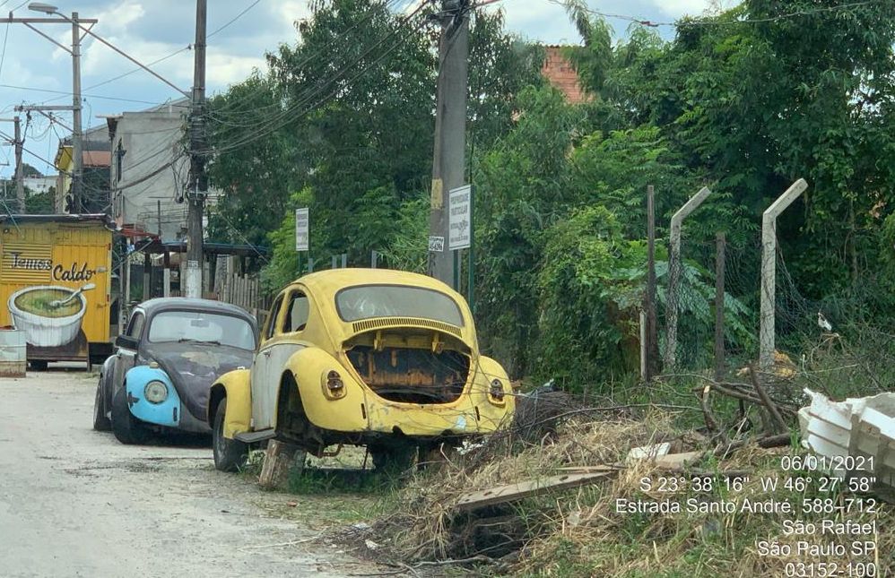 Dois fuscas, um amarelo e outro preto estão em uma rua, identificada como Estrada Santo André, Parque São Rafael. A Lataria está danificada. O amarelo está sem a tampa do motor.  