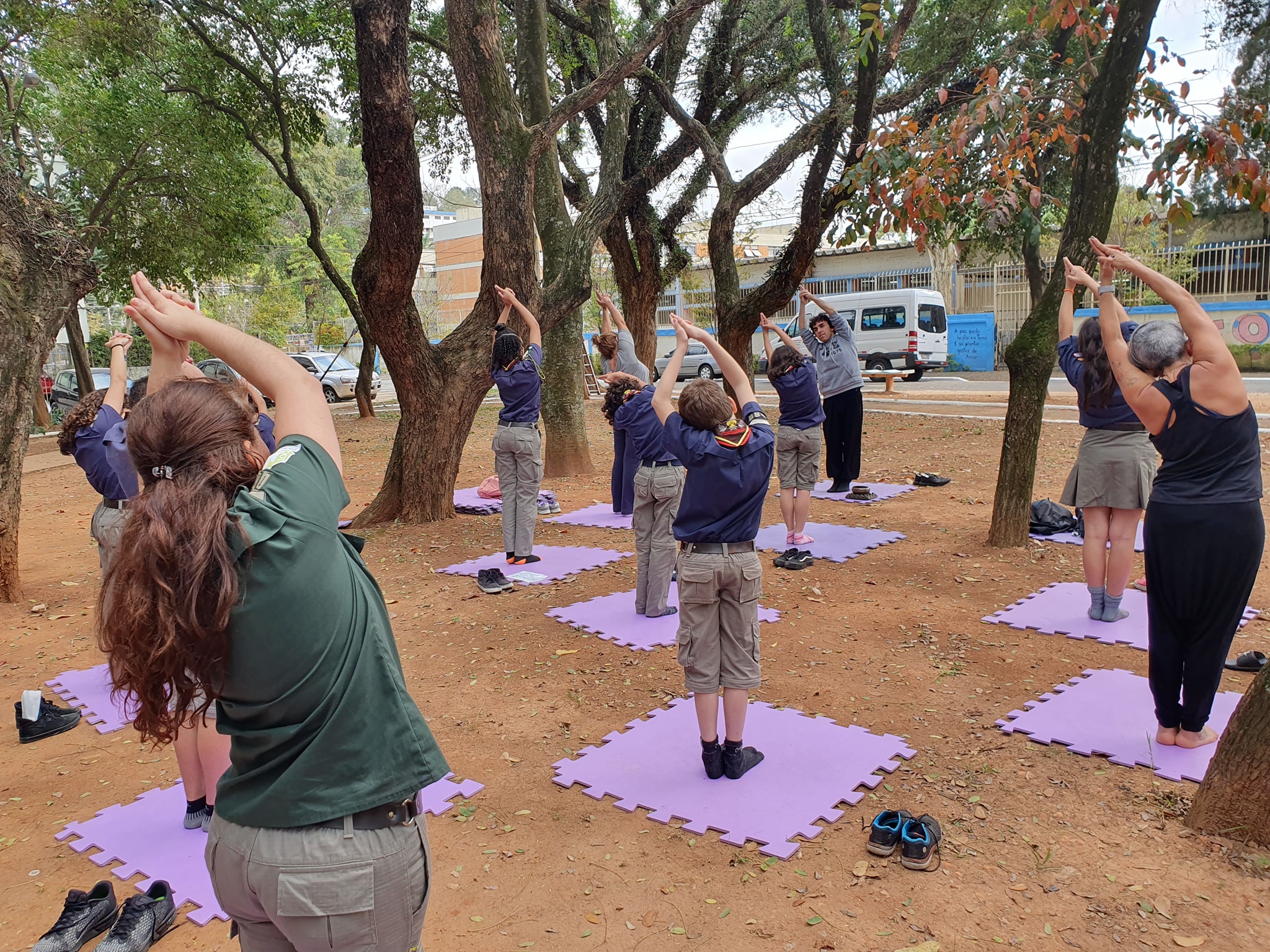 Imagem colorida, com cerca de 10 pessoas, fazendo aula de Yoga em uma praça.