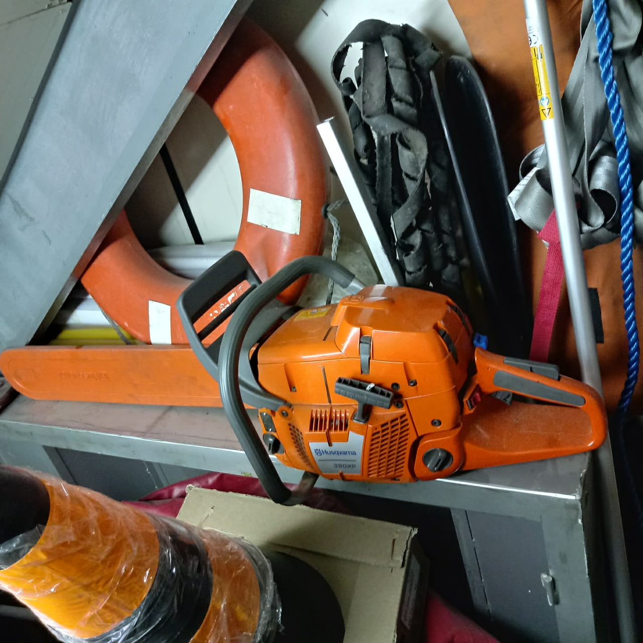 Uma motoserra laranja, cones de isolamento de trânsito e passagem e uma boia de salvamento estão guardados em um compartimento pequeno.