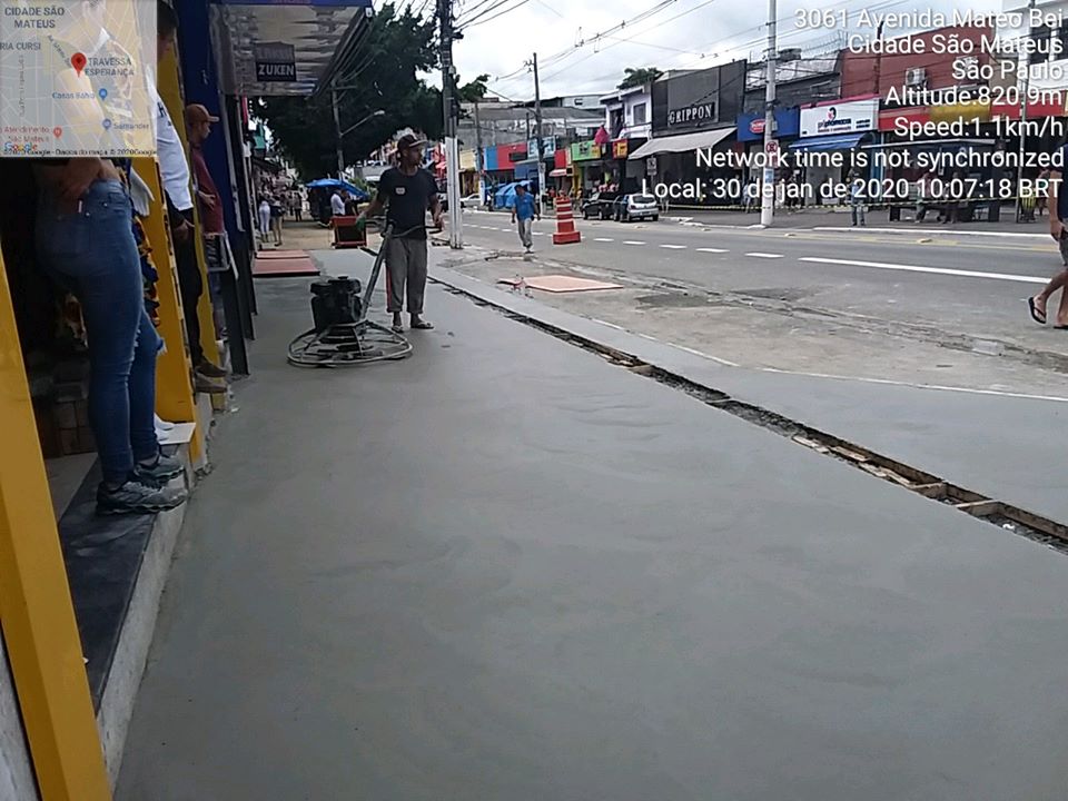Homem passa máquina de alisar cimento em uma calçada. Foto identifica como Avenida Mateo Bei