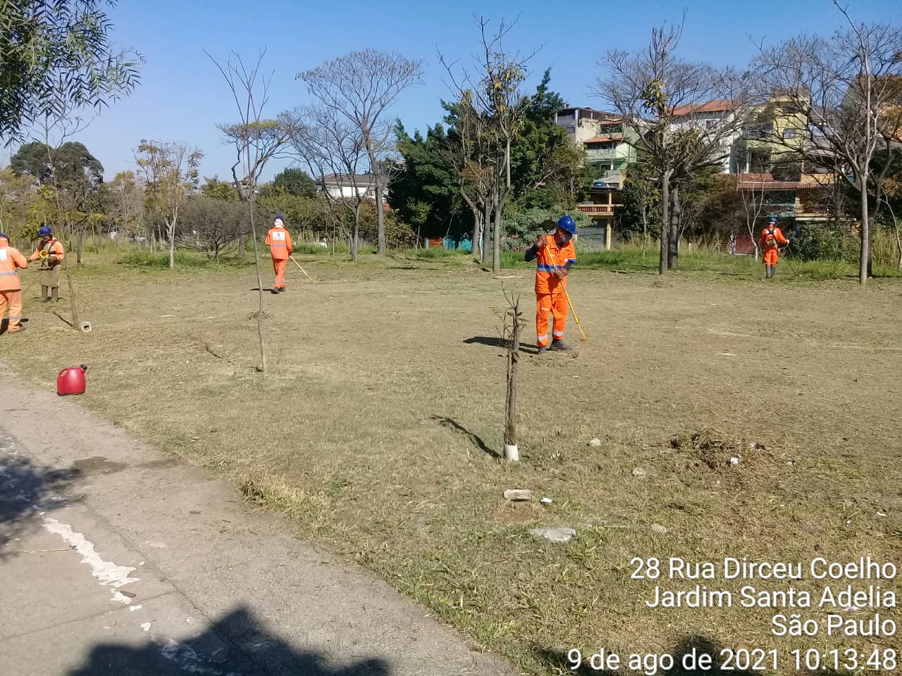 Trabalhadores com uniforme laranja trabalham no corte de grama em uma praça. Foto identificada como sendo rua Dirceu Coelho, Jardim Santa Adélia. 