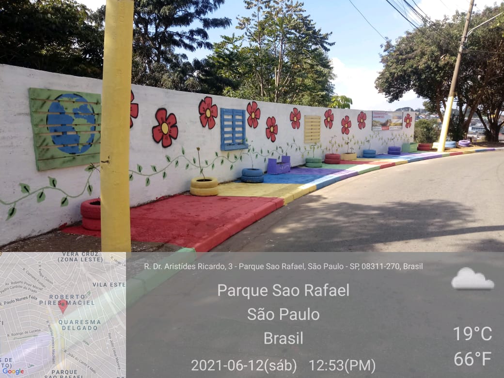 Em um muro pintado de branco, desenhos de flores coloridas. A calçada também foi pintada com cores fortes, sobressaindo o vermelho e o azul. 