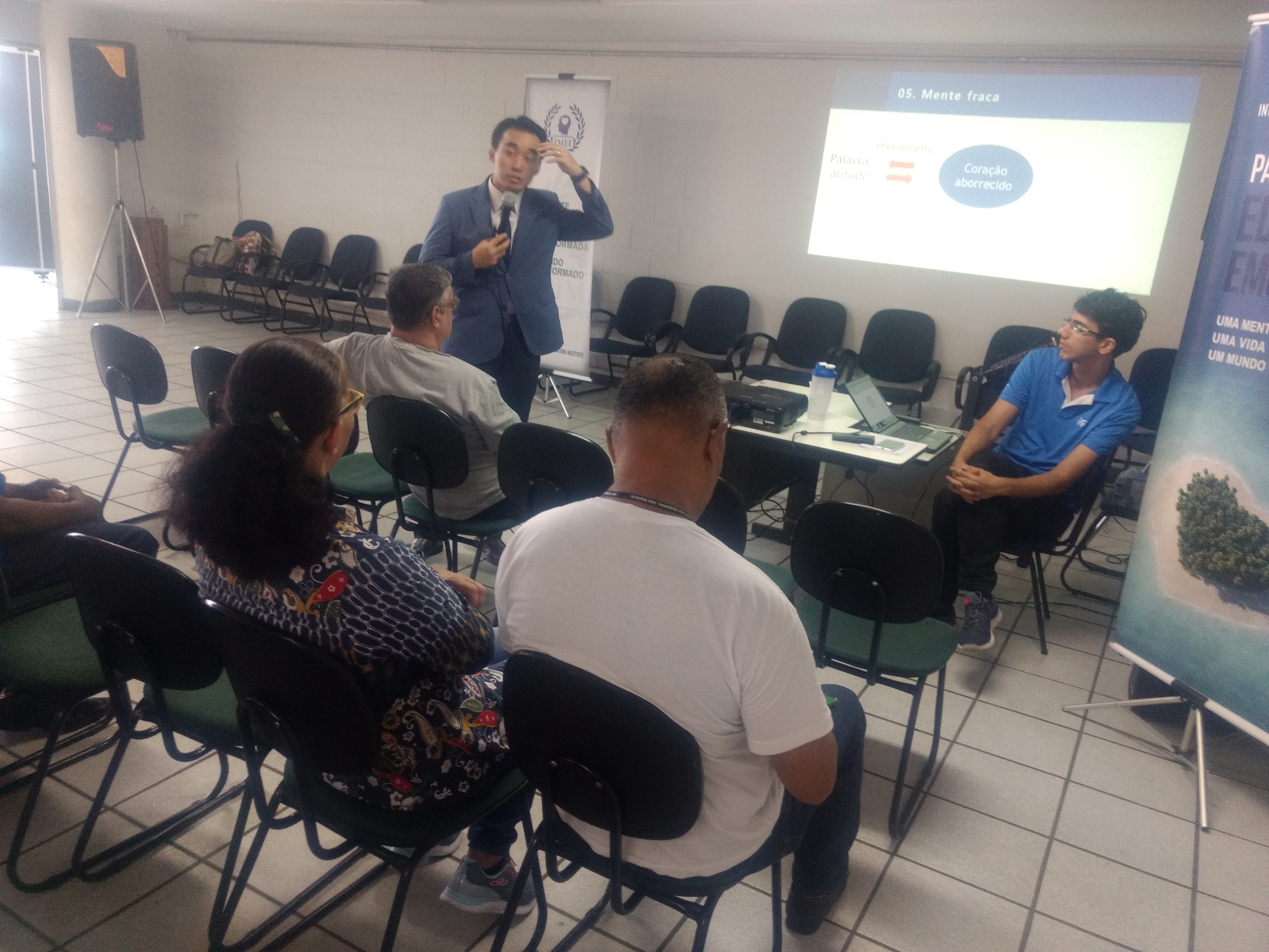 Daniel Jo, de terno e gravata, dá palestra para funcionários da prefeitura, que estão sentados.