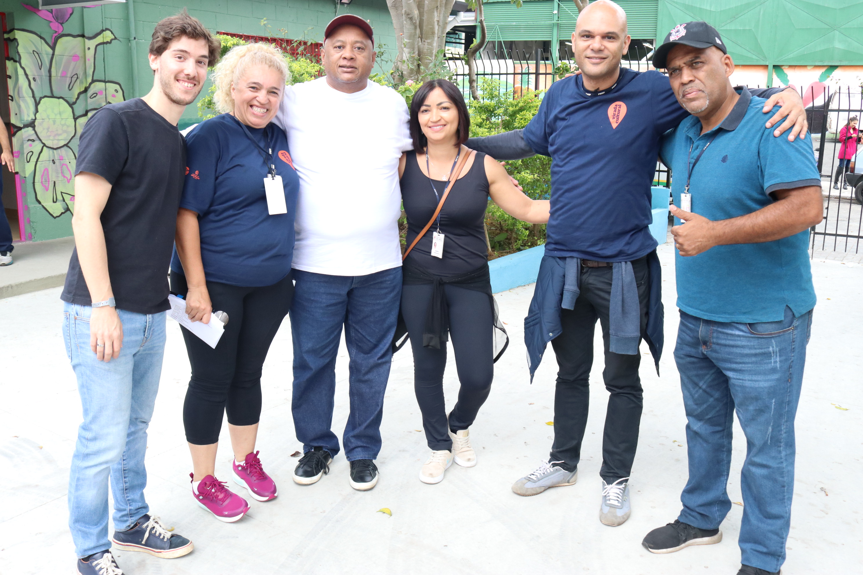 duas mulheres e quatro homens abraçados lado a lado em frente a entrada da casa de cultura mboi mirim