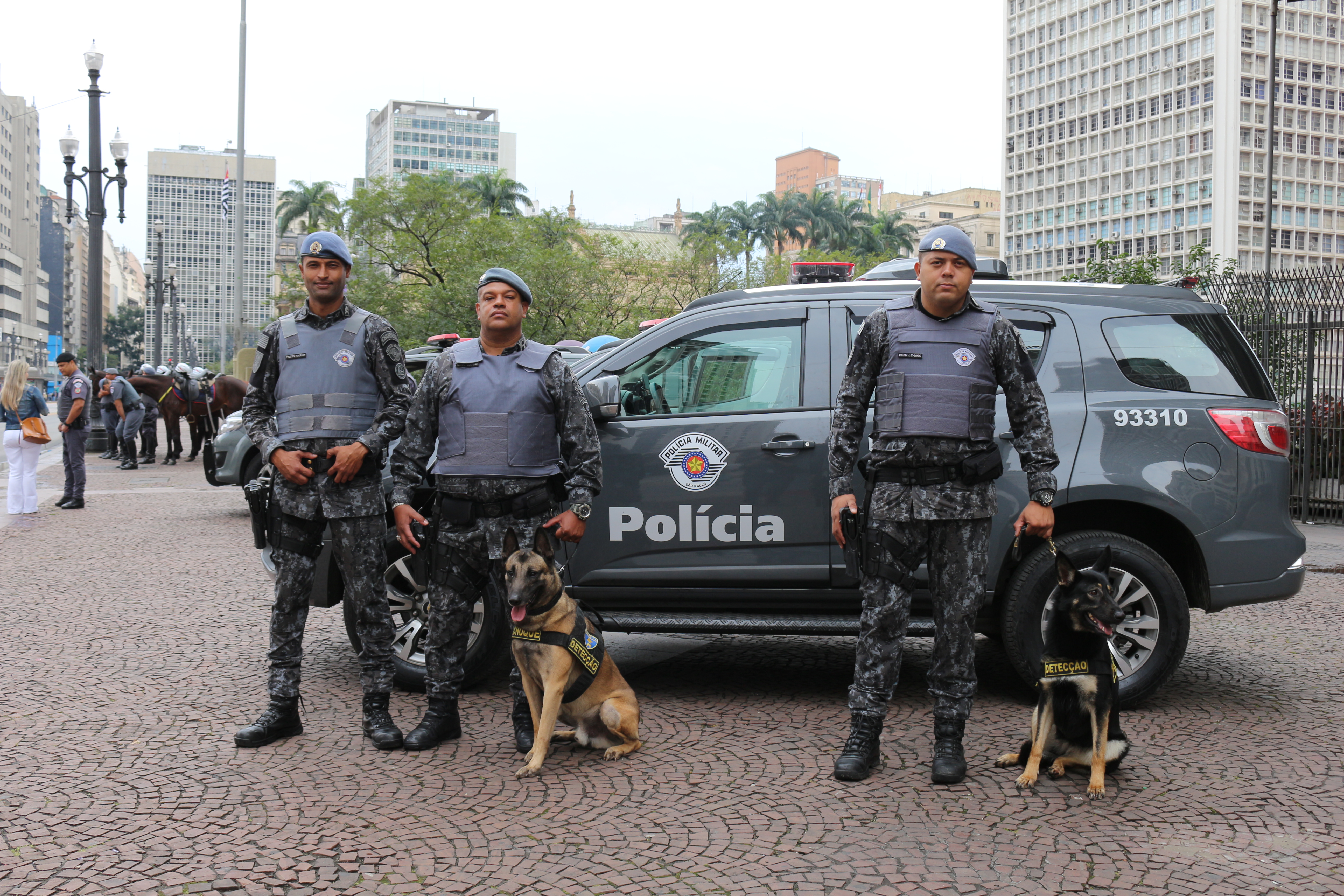 Foto colorida mostra três policiais e dois cachorros do Canil da PM