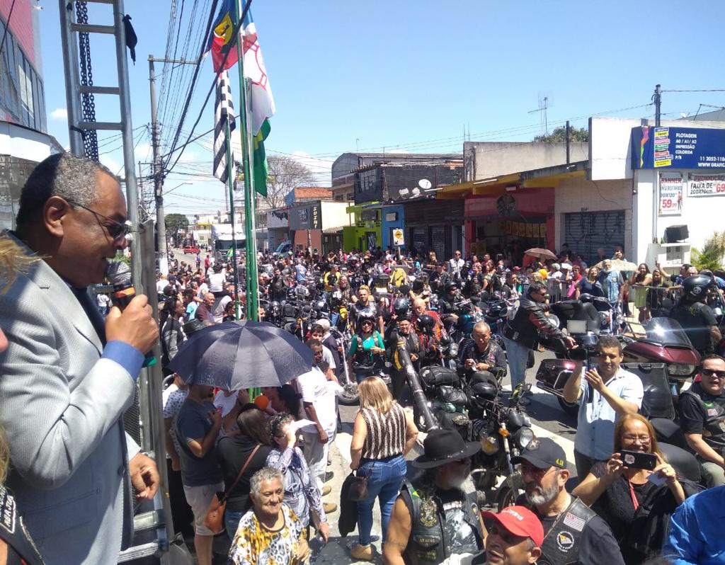 A imagem mostra o Subprefeito Edson Marques em cima do palco e ao fundo uma grande fila de componentes de Moto Clubes.