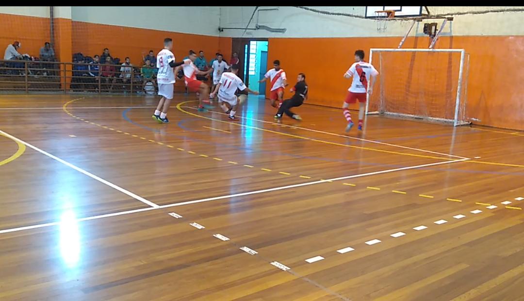 Na imagem sete jogadores disputam uma partida de futsal e ao fundo, torcedores assistem a partida. 