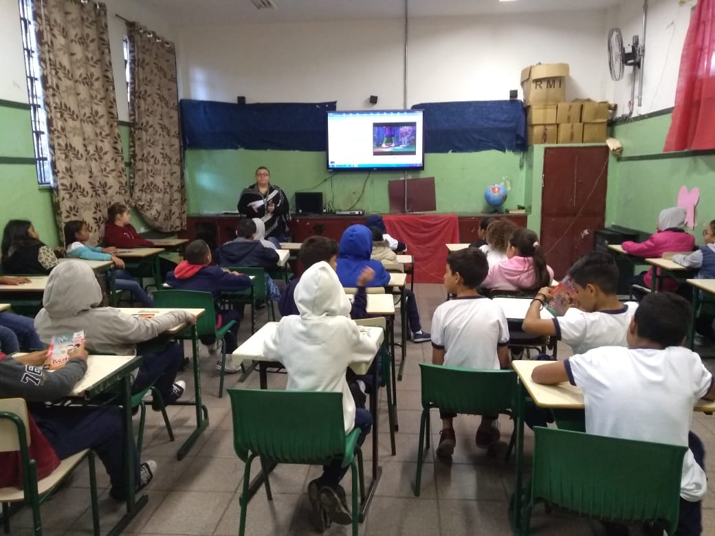 Alunos estão sentados na sala de aula assistindo a um vídeo