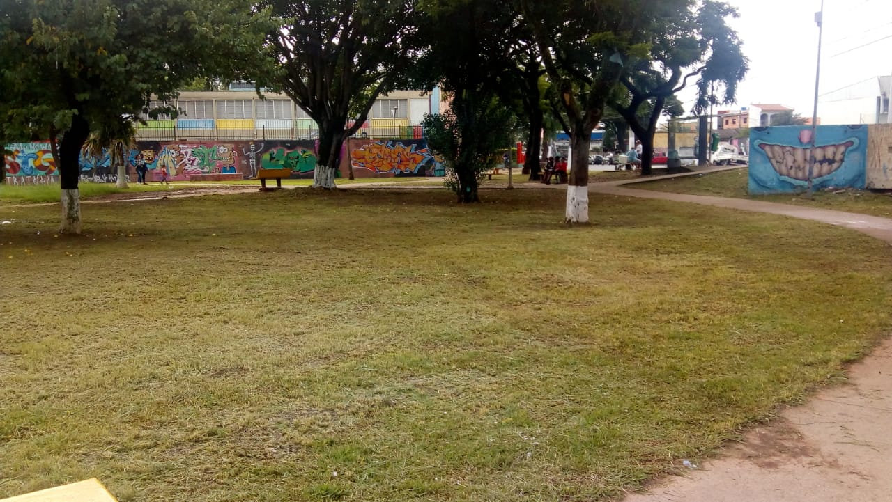 Em plano geral aberto a Praça Craveiro do Campo após os serviços de zeladoria, como corte de grama. Ao fundo da foto existe um muro completamente colorido de grafiti. 