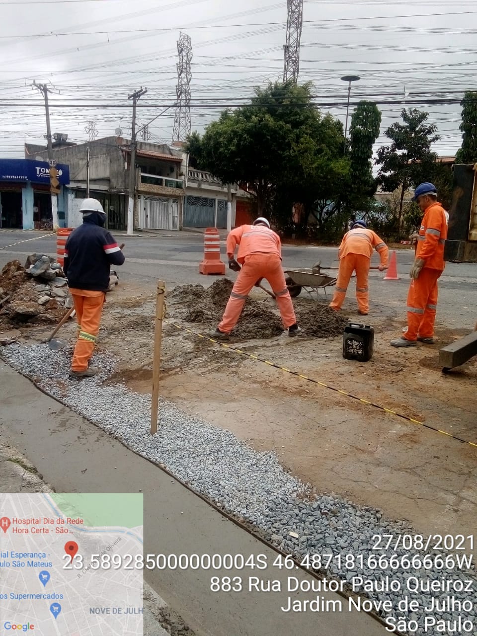 Quatro homens trabalham na concretagem de uma canaleta de concreto. Um deles enche um carrinho de mão e o ouytro está com uma enxada raspando um monte de terra sobre o asfalto. Na rua Doutor Paulo Queiroz, 883, no Jardim 9 de Julho. 