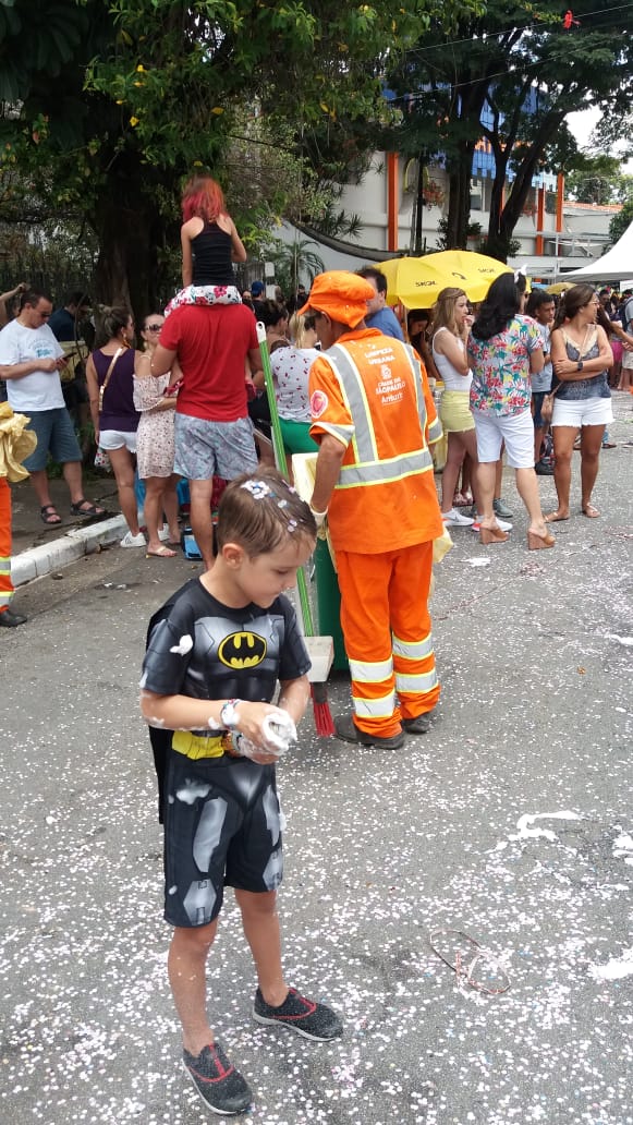 #PraCegoVer visualiza-se a imagem de uma criança vestida de Batman jogando confete e espuma no Carnaval de rua.