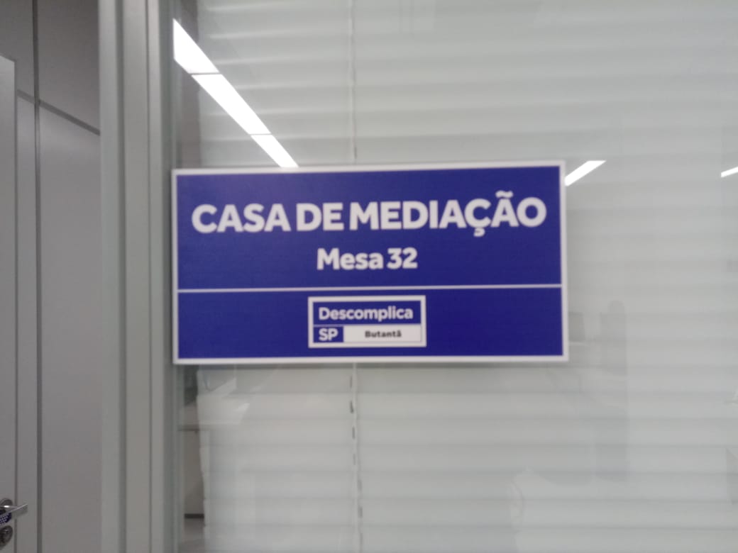 Placa da Casa de Mediação em azul, com textos escritos em cor branca. Na placa é demonstrado o logo do Descomplica Butantã.     