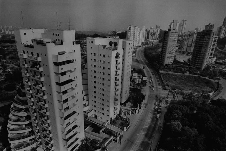 A imagem, em preto e branco, mostra uma vista aérea da avenida Giovanni Gronchi. A via é cercada por prédios em ambos os lados. Ao lado direito também há áreas de vegetação.
