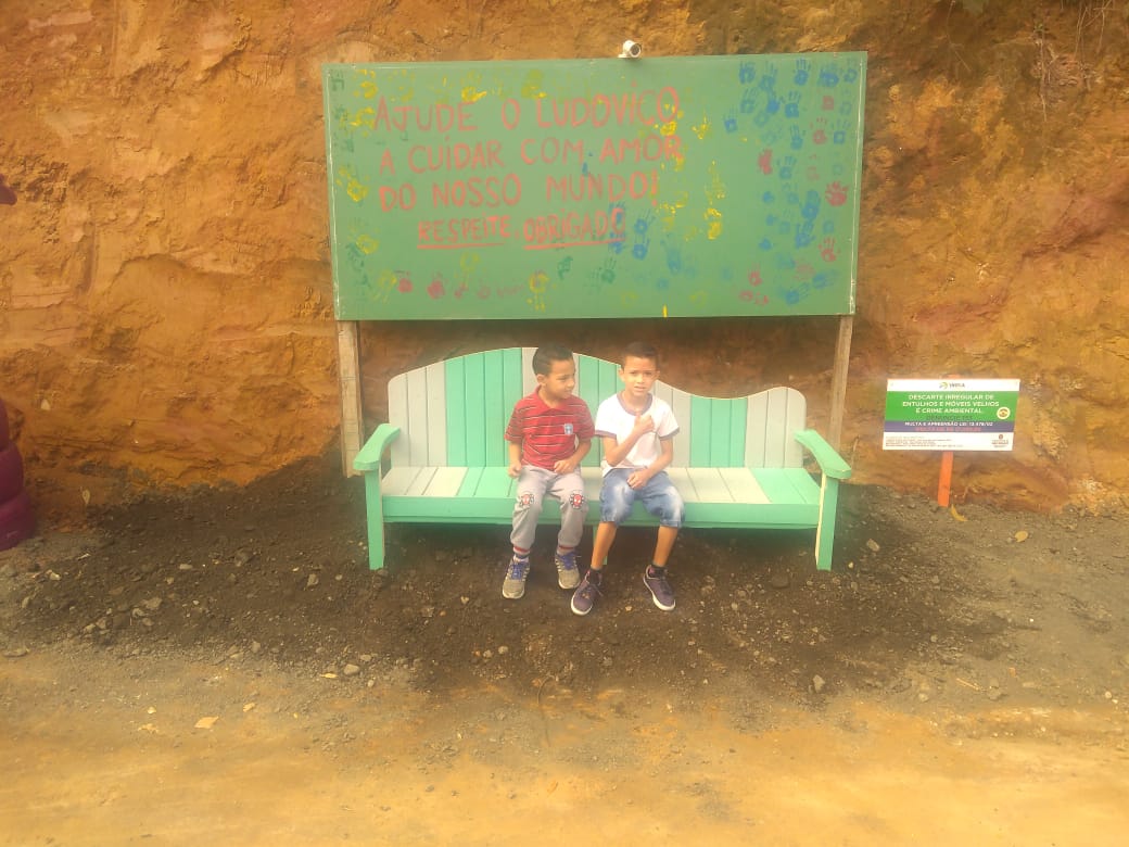 Duas crianças sentadas em um banco colocado no local revitalizado.