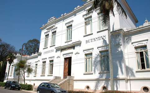 A imagem retrata um edifício de dois andares, com paredes brancas e elementos arquitetônicos típicos do final do século XIX. Há muitas janelas na fachada, além de uma pequena escada no centro do prédio que leva até a porta de madeira. No canto inferior esquerdo, pode-se observar algumas árvores e carros parados na calçada. Já no lado oposto há uma palmeira alta. 