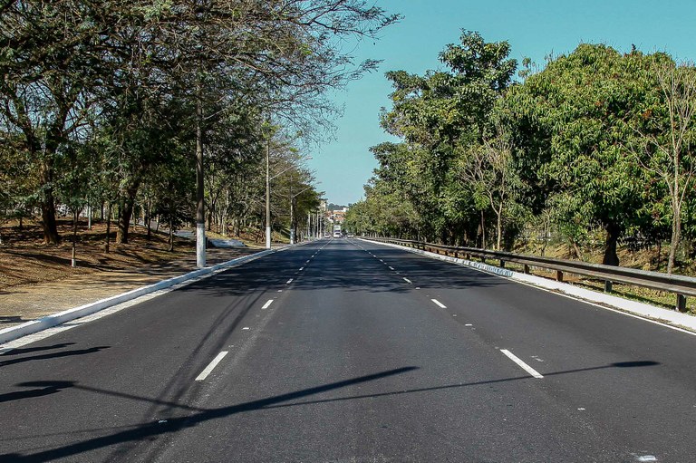 Foto tirada na pista da Avenida Politécnica após a conclusão do recapeamento, a foto é de profundidade, capturando um grande trecho da Avenida. A massa asfáltica após o recapeamento possuí uma cor mais escura, diferente da massa asfáltica comum que tem uma cor cinza claro. Nenhuma deformidade é vista no asfalto por toda a extensão capturada na foto.