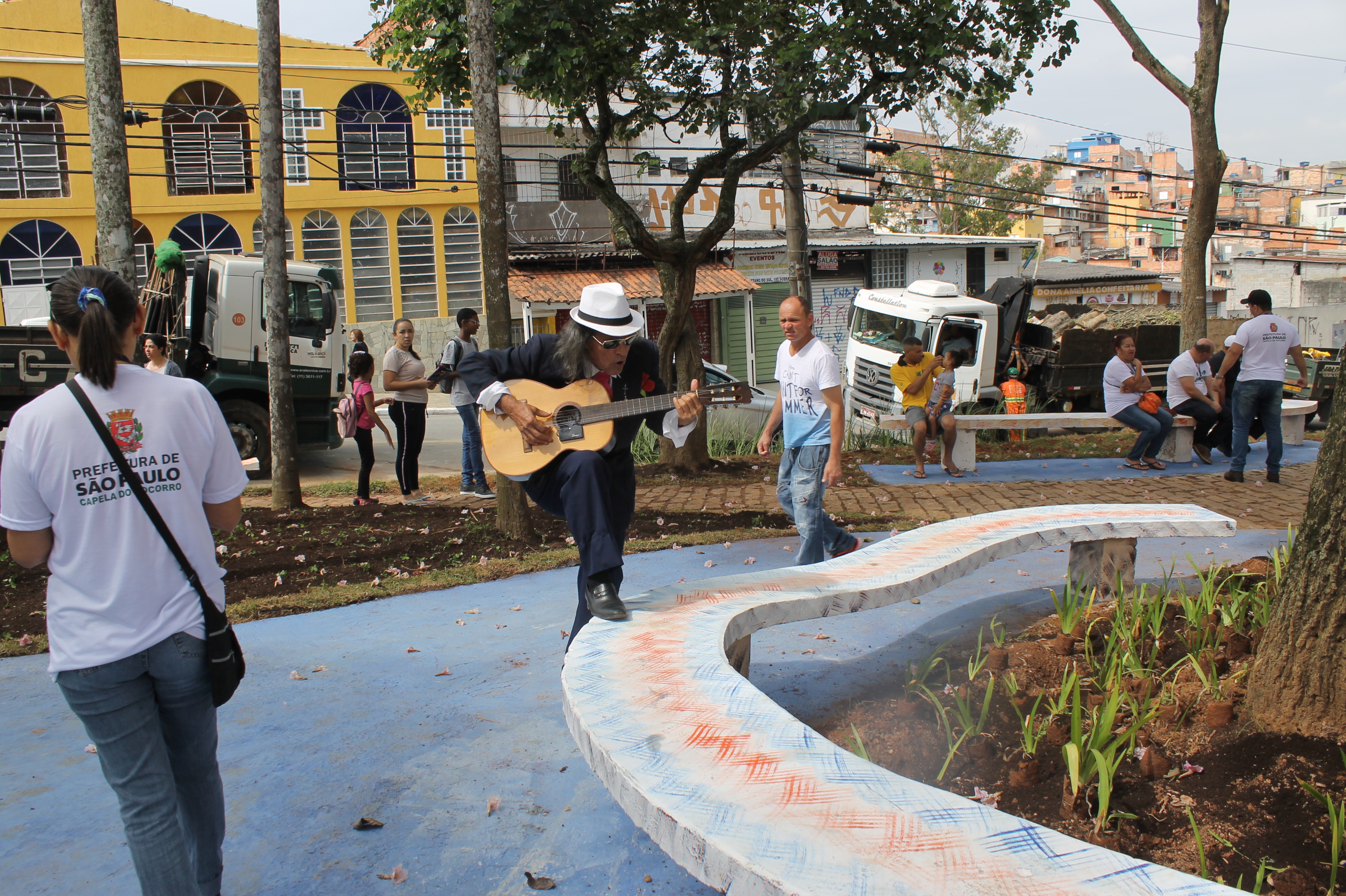 #PraCegoVer - Santana Batista, chamado o "Roberto Carlos do Grajaú", toca violão na praça Dois Corações. Santana usa chapéu e apoia o pé em um banco da praça.