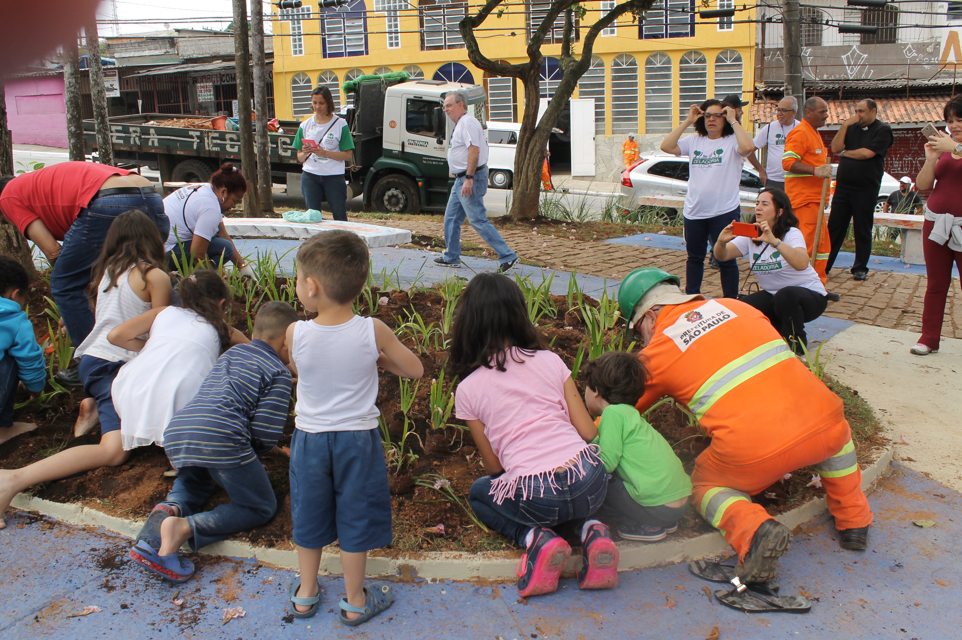 #PraCegoVer - Crianças moradoras no entorno da praça ajudam a plantar mudas de flores nos canteiros da nova praça.