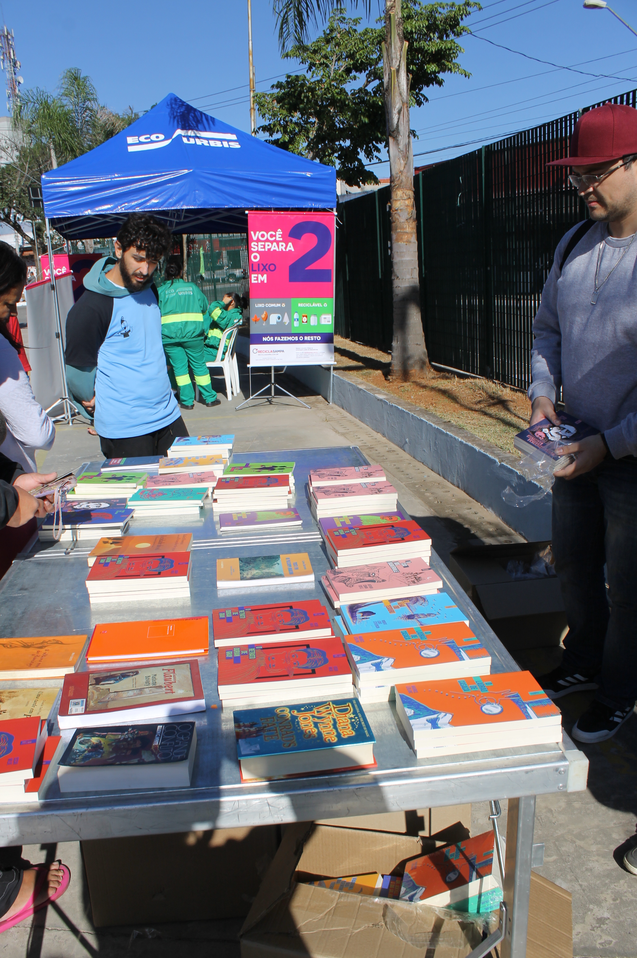 #PraCegoVer - Banca de livros para doação à população no dia do Mutirão nos Bairros na Vila São José. Os livros estão dispostos em uma mesa-tabuleiro para exame das pessoas.