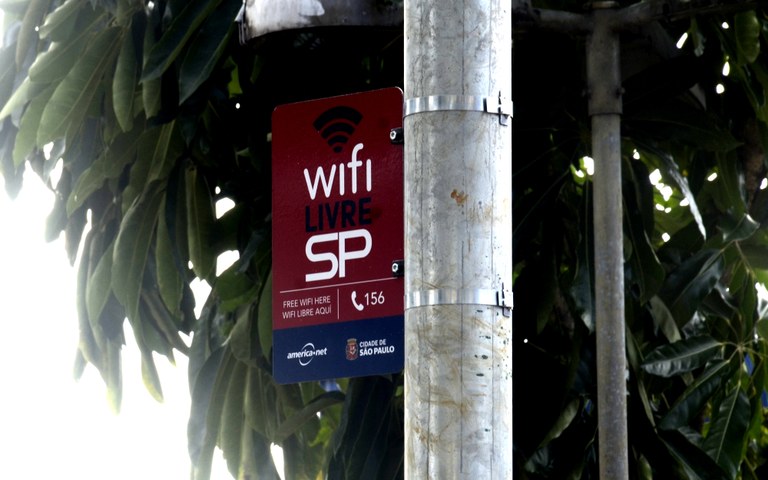 #PraCegoVer - foto de poste com placa fixada, na placa há o símbolo do wifi.