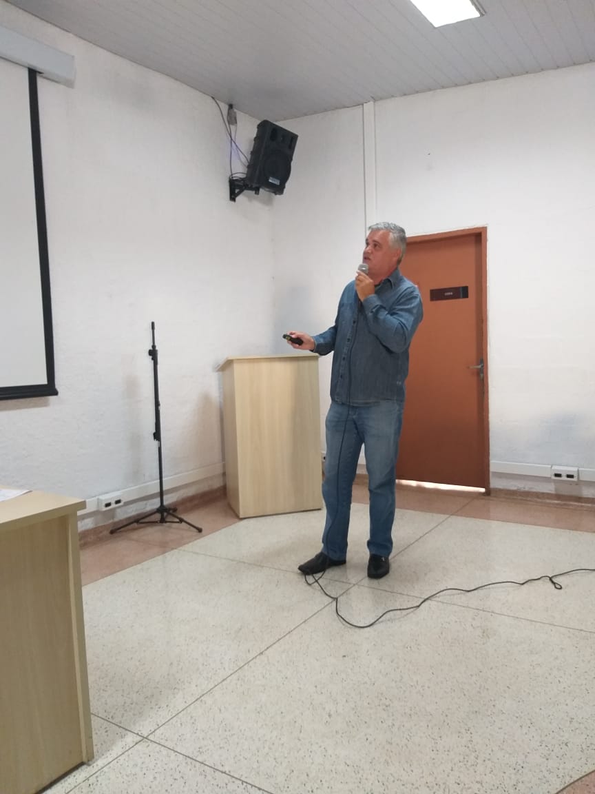 #PraCegoVer - Palestrante Lúcio Deodato na sala multiuso da Subprefeitura. O palestrante está com o microfone. Veste camisa e calças jeans. Ao fundo, na parede, há um alto-falante.