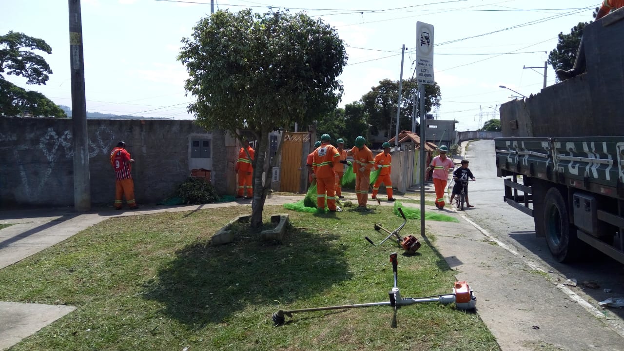 #PraCegoVer - Praça Chico Vieira - Jardim Shangrilá: grama já cortada, os trabalhadores da Subprefeitura ao fundo. Em primeiro plano, vê-se um cortador motorizado de grama.