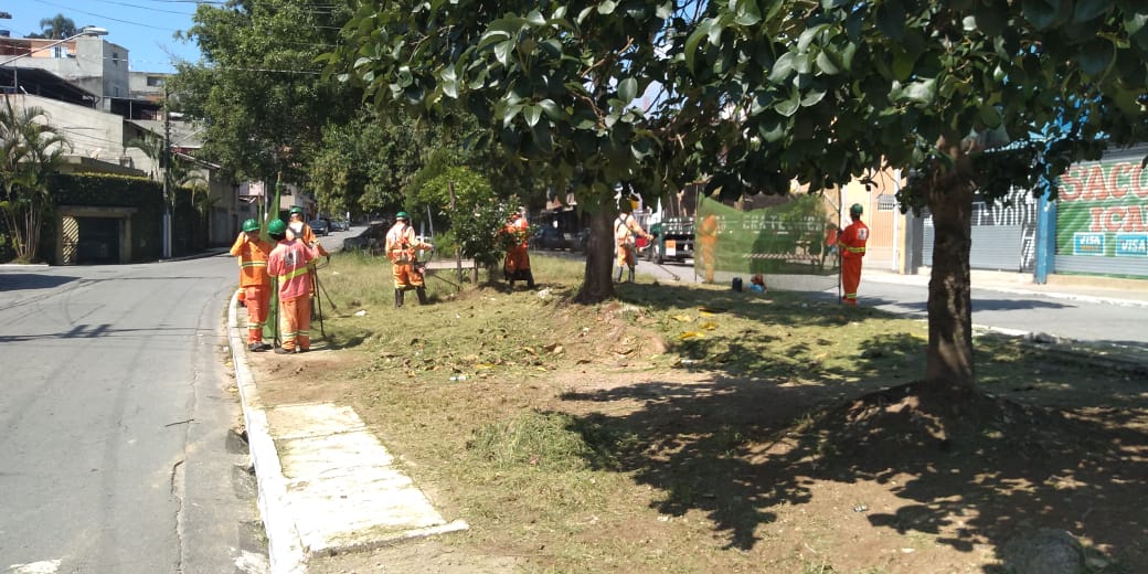 #PraCegoVer - Trabalhadores cortam grama nos canteiros dos dois lados do passeio