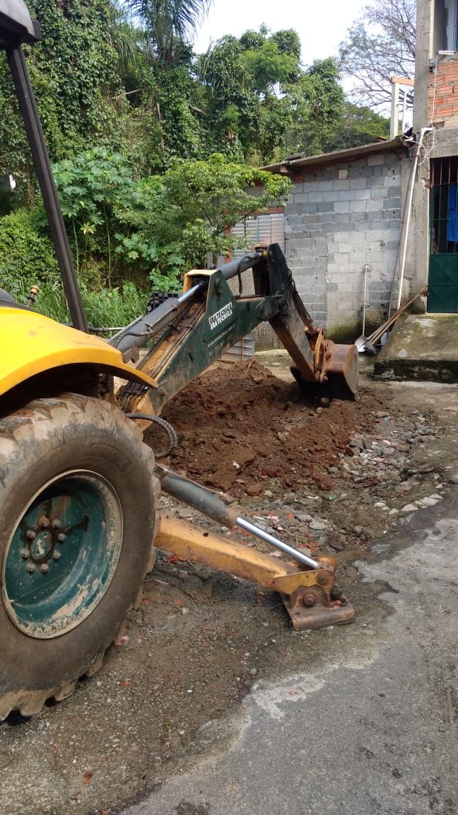 #PraCegoVer - Escavadeira a serviço da Subprefeitura abre o local em que serão cimentados a sarjeta nova e o sarjetão (junção de ruas)