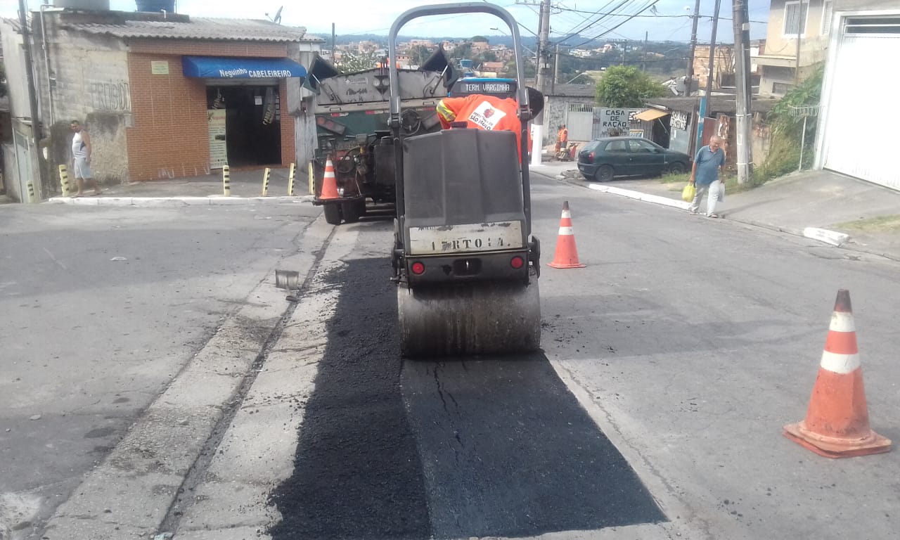 #PraCegoVer - Máquina compactadora de asfalto, finalizando conserto de buraco na via. No segundo plano, um caminhão da empresa contratada.