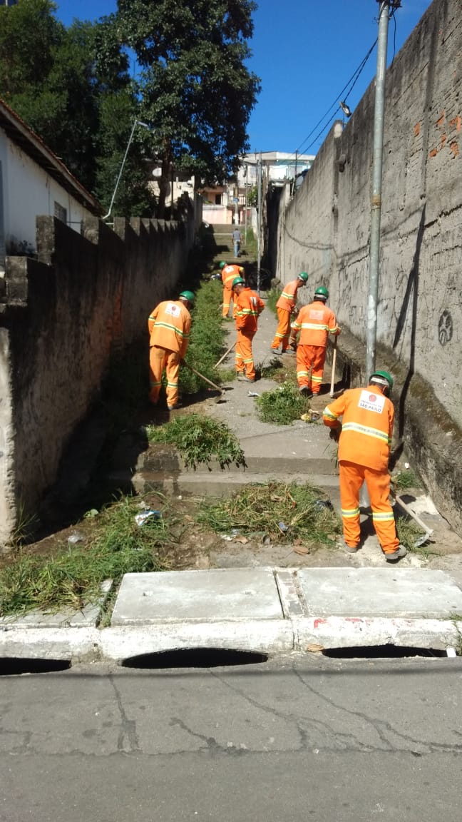 #PraCegoVer - Trabalhadores da Subprefeitura em macacões laranja e branco iniciando capinação para futura reforma do escadão