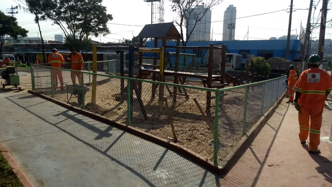 #PraCegoVer - Na praça, os trabalhadores concluem instalação de alambrado de proteção ao brinquedo Casa do Tarzan — uma casinha com escada e escorregador.